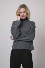 Das Model trägt einen Stehkragenpullover von Luisa Cerano und eine anthrazitfarbene, karierte Hose von Cambio.