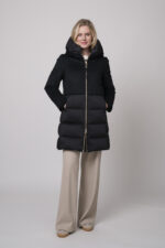 Das Model trägt eine schwarze Daunenjacke von Duno und dazu eine sandfarbene Hose von Cambio.