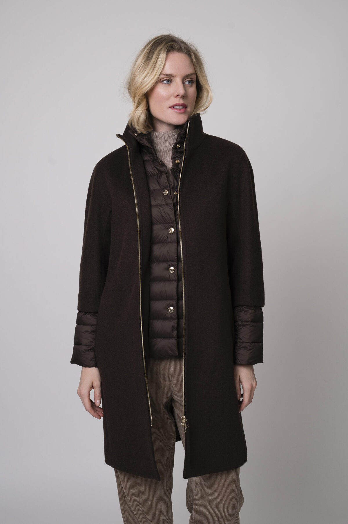 Das Model trägt einen Stehkragenpullover von Hemisphere in Sand, dazu eine Cordhose von Cambio in Camel und einen braunen Mantel von Joop.