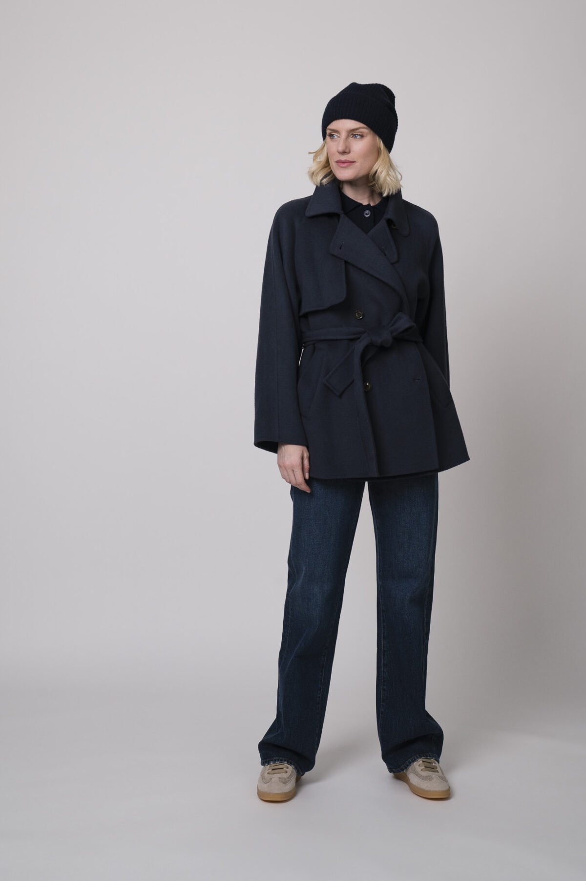 Das Model trägt eine marineblaue Jacke von Helmur, eine Jeans von 7 for all mankind sowie eine Strickweste von True Religion in Marine und eine Haube von FFC.