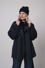 Das Model trägt eine marineblaue Jacke von Helmur, eine Jeans von 7 for all mankind sowie eine Strickweste von True Religion in Marine und eine Haube von FFC.