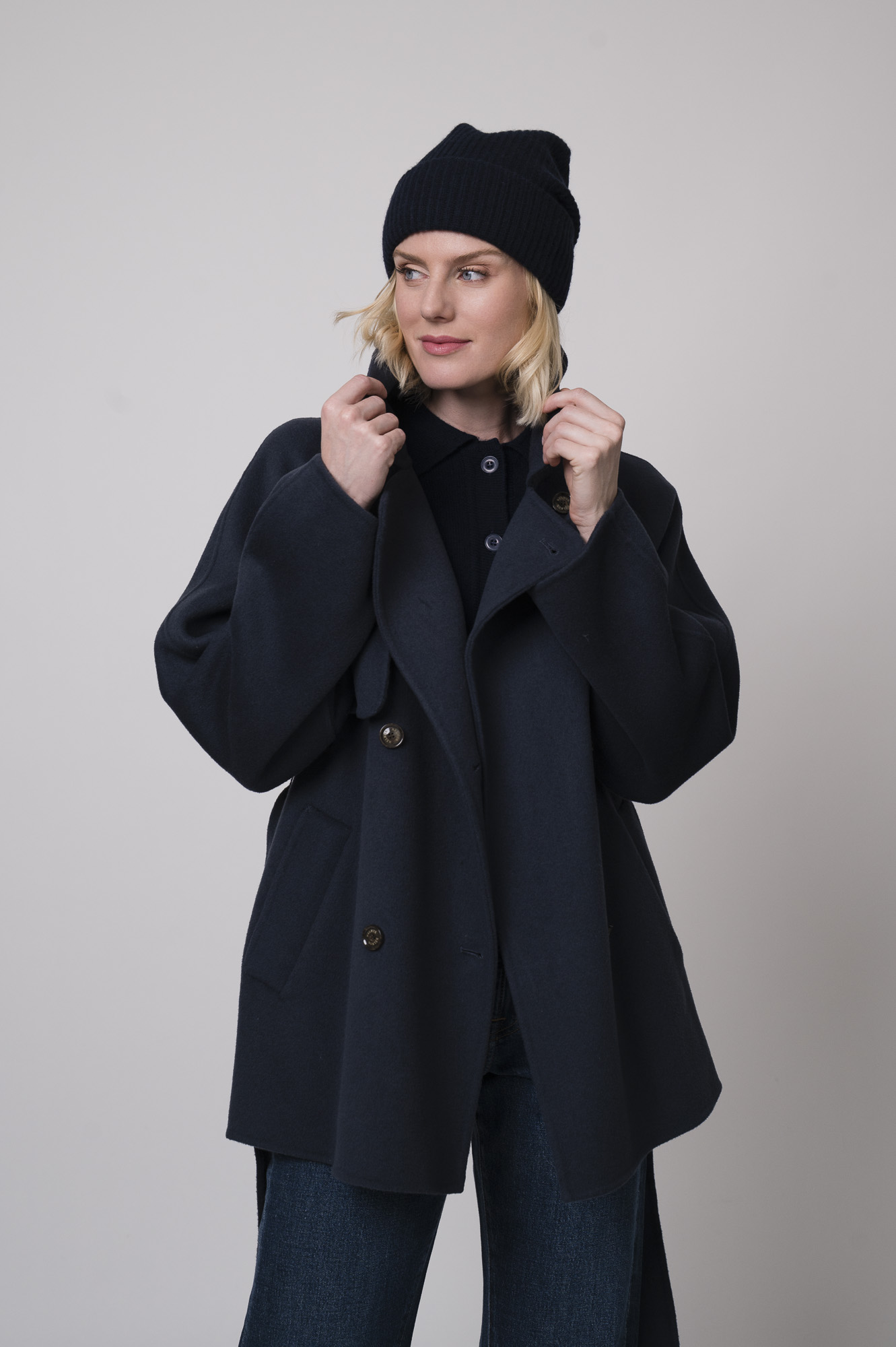 Das Model trägt eine marineblaue Jacke von Helmur, eine Jeans von 7 for all mankind sowie eine Strickweste von True Religion in Marine und eine Haube von FFC.