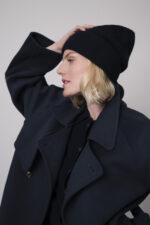 Das Model trägt eine marineblaue Jacke von Helmur, eine Jeans von 7 for all mankind sowie eine Strickweste von True Religion in Marine und eine Haube von FFC.