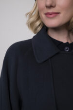 Das Model trägt eine marineblaue Jacke von Helmur, eine Jeans von 7 for all mankind sowie eine Strickweste von True Religion in Marine und eine Haube von FFC.