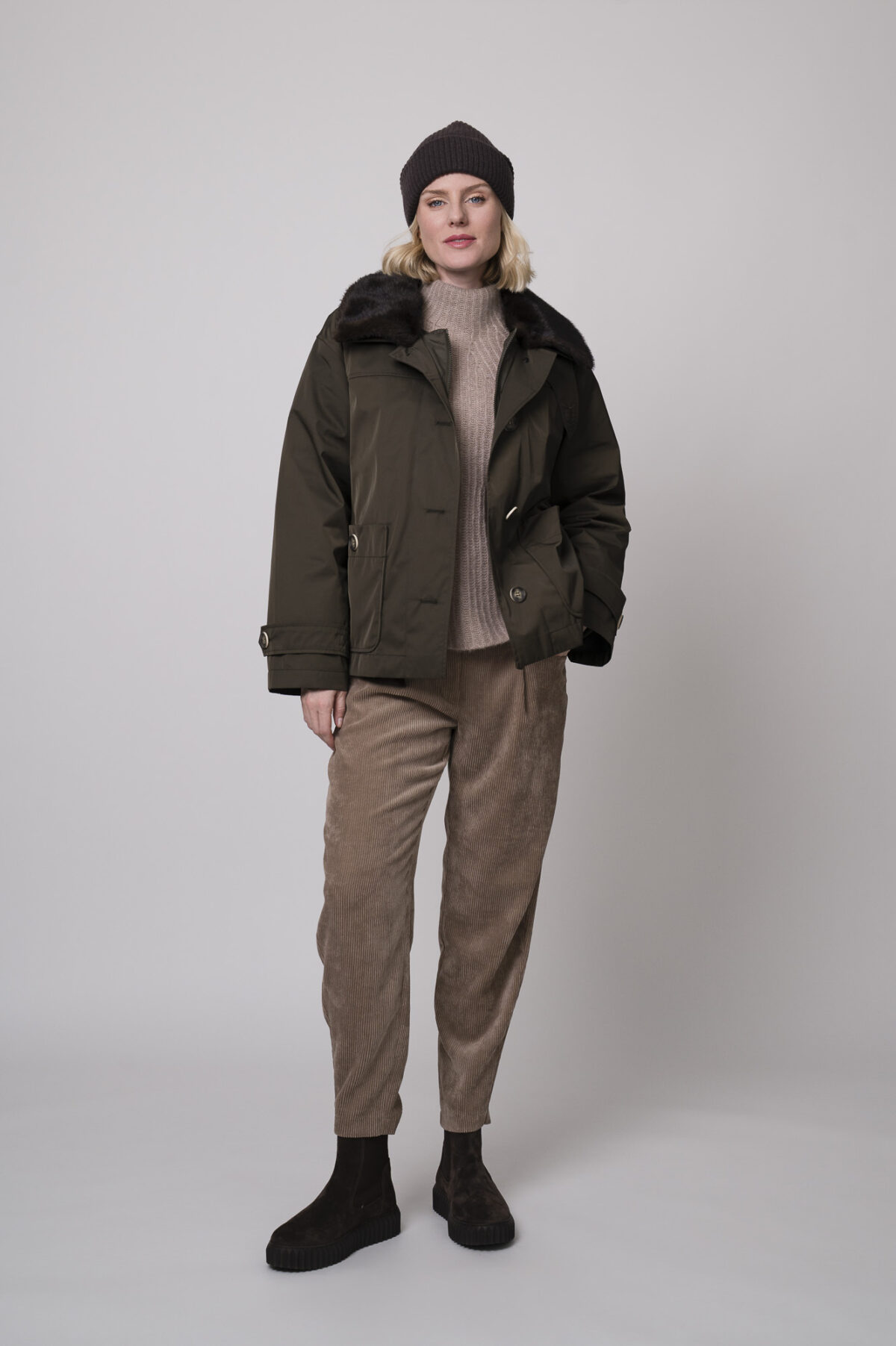 Das Model trägt eine Jacke von Lou Andrea, eine Cordhose von Cambio in Camel, einen Stehkragenpullover von Hemisphere in Sand sowie eine Haube von FFC.