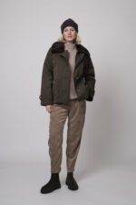 Das Model trägt eine Jacke von Lou Andrea, eine Cordhose von Cambio in Camel, einen Stehkragenpullover von Hemisphere in Sand sowie eine Haube von FFC.