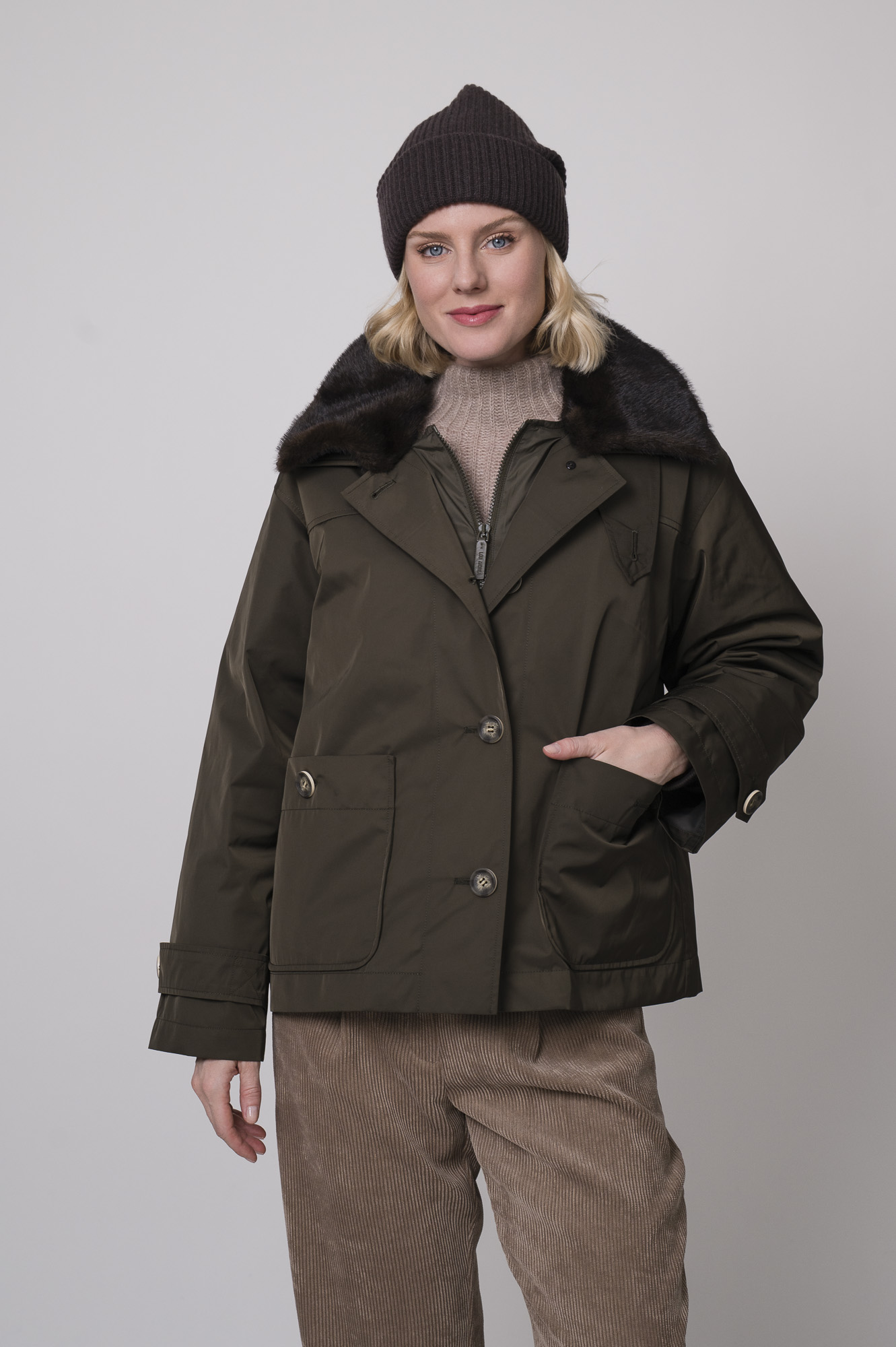 Das Model trägt eine Jacke von Lou Andrea, eine Cordhose von Cambio in Camel, einen Stehkragenpullover von Hemisphere in Sand sowie eine Haube von FFC.