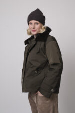 Das Model trägt eine Jacke von Lou Andrea, eine Cordhose von Cambio in Camel, einen Stehkragenpullover von Hemisphere in Sand sowie eine Haube von FFC.