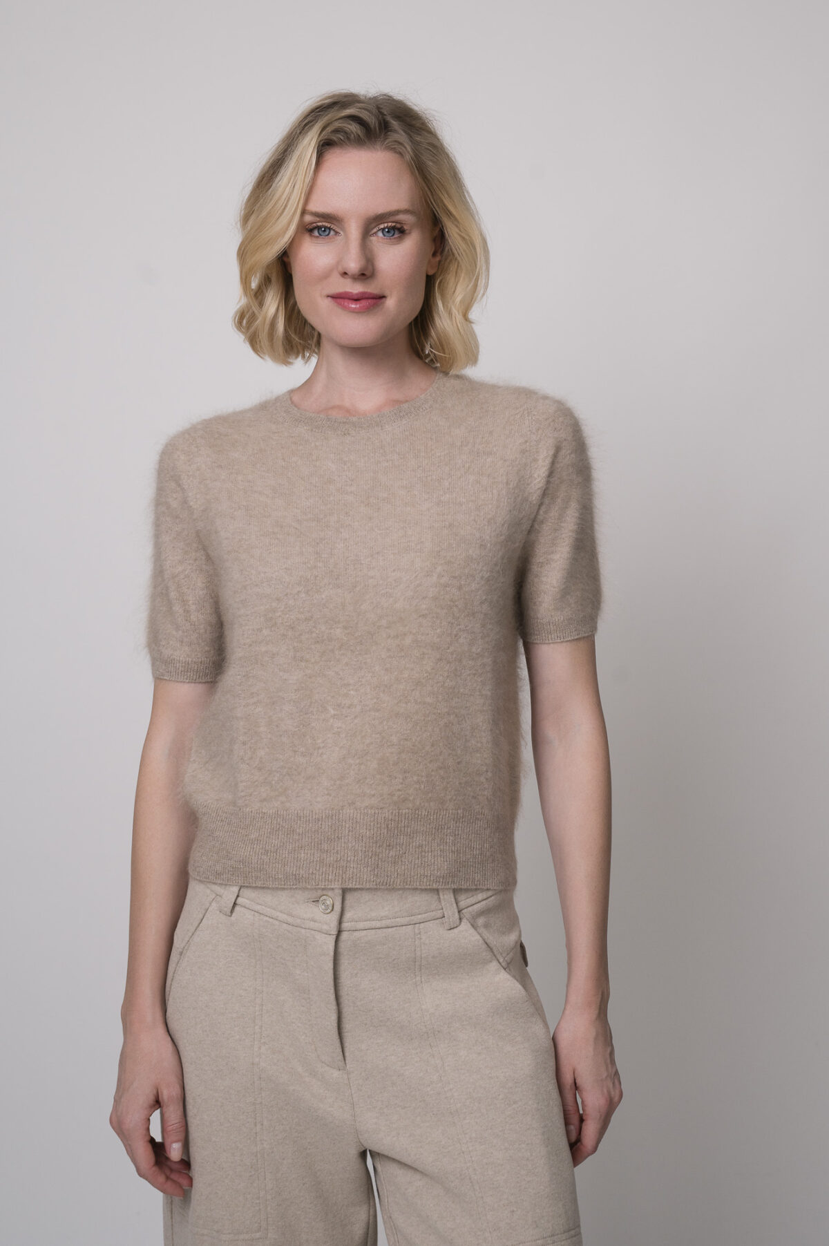 Das Model trägt eine sportliche Hose von Cambio in Sand sowie einen Camel-Pullover von Absolut Cashmere.