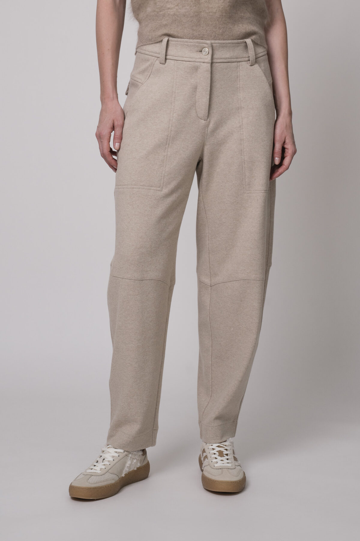 Das Model trägt eine sportliche Hose von Cambio in Sand sowie einen Camel-Pullover von Absolut Cashmere.