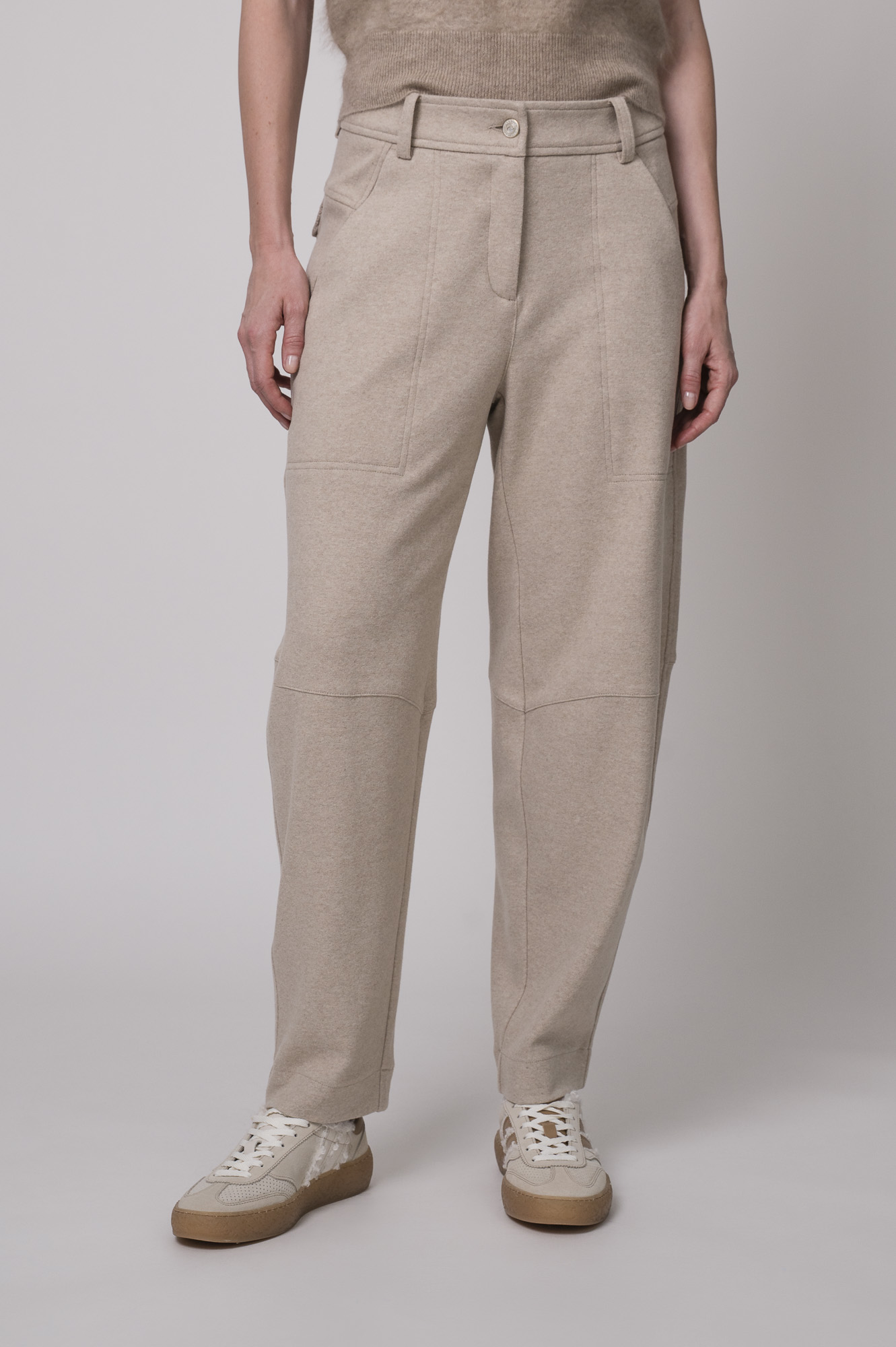 Das Model trägt eine sportliche Hose von Cambio in Sand sowie einen Camel-Pullover von Absolut Cashmere.