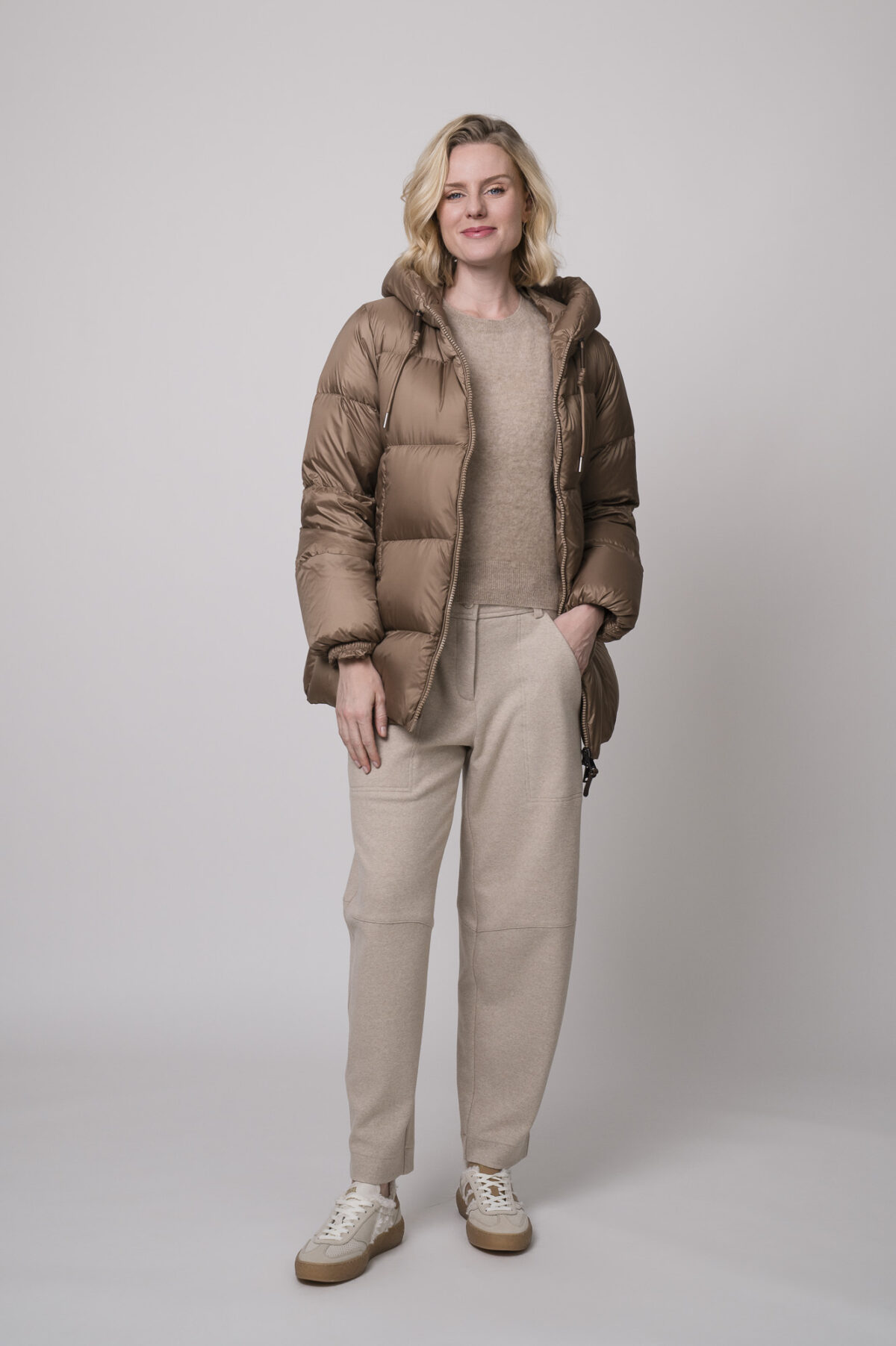 Das Model trägt eine camelfarbene Daunenjacke von Mabrun, eine sandfarbene Hose von Cambio und einen Camel-Pullover von Absolut Cashmere.