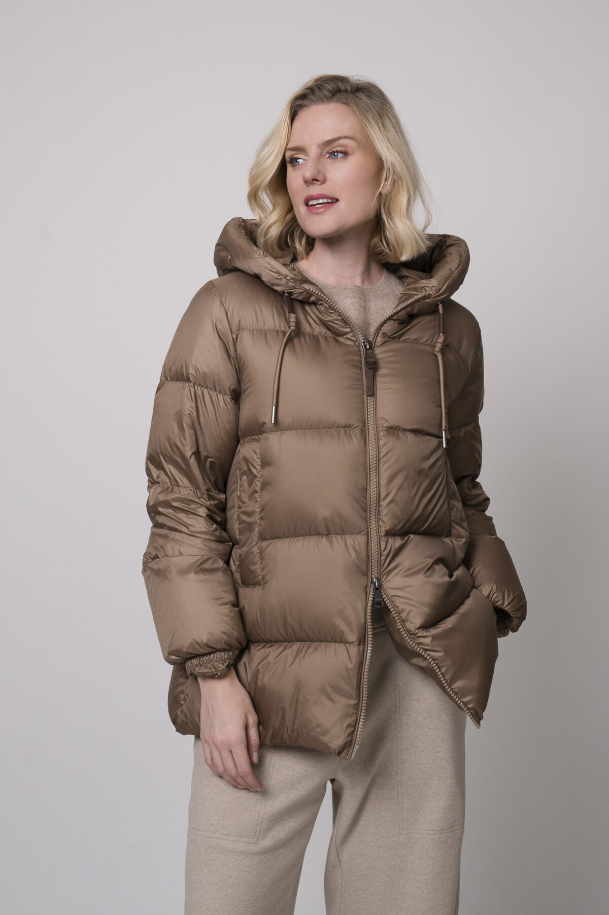 Das Model trägt eine camelfarbene Daunenjacke von Mabrun, eine sandfarbene Hose von Cambio und einen Camel-Pullover von Absolut Cashmere.