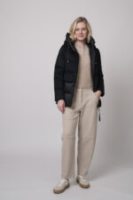 Das Model trägt eine schwarze Daunenjacke von Duno, eine sandfarbene Hose von Cambio und einen Pullover von Absolut Cashmere in Camel.