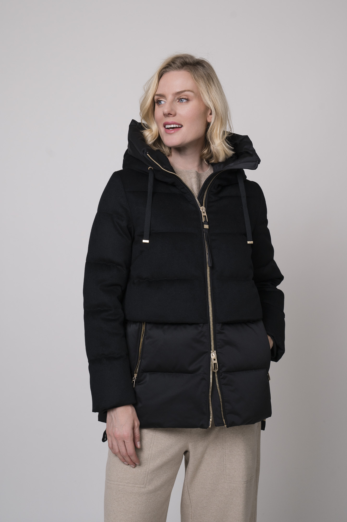 Das Model trägt eine schwarze Daunenjacke von Duno, eine sandfarbene Hose von Cambio und einen Pullover von Absolut Cashmere in Camel.