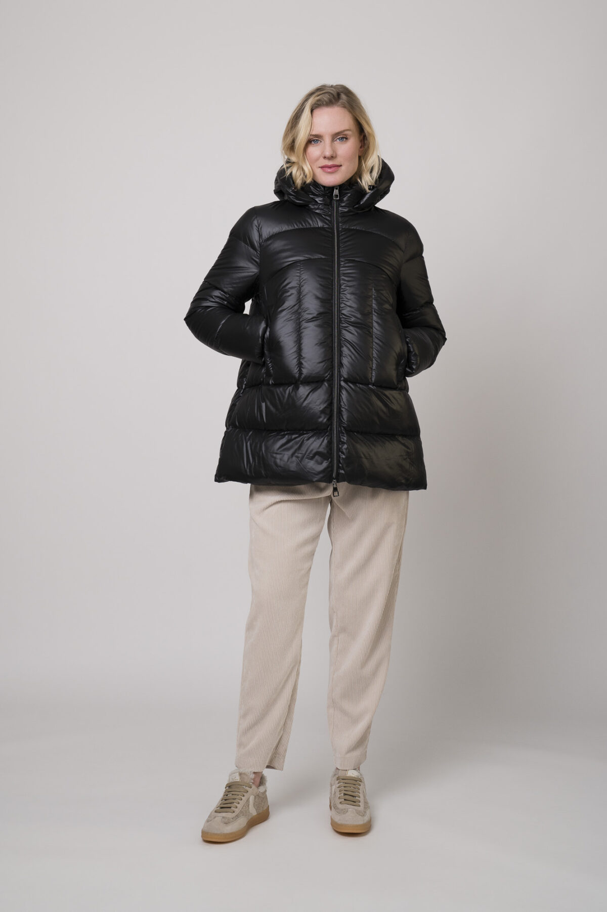 Das Model trägt eine Daunenjacke von Helmur in Mittelblau sowie eine Cordhose von Camio in der Farbe Sand und Sneaker von Voile Blanche.