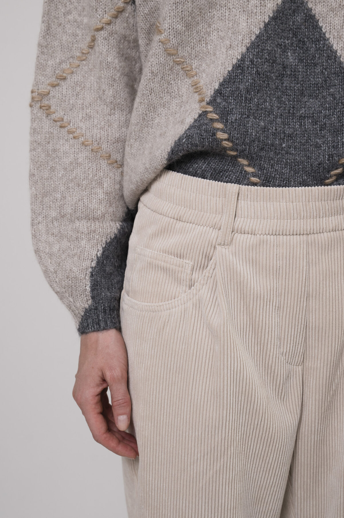 Das Model trägt einen Pullover von Luisa Cerano mit Rautenmuster in Anthrazit sowie eine Cordhose von Cambio in Natur.