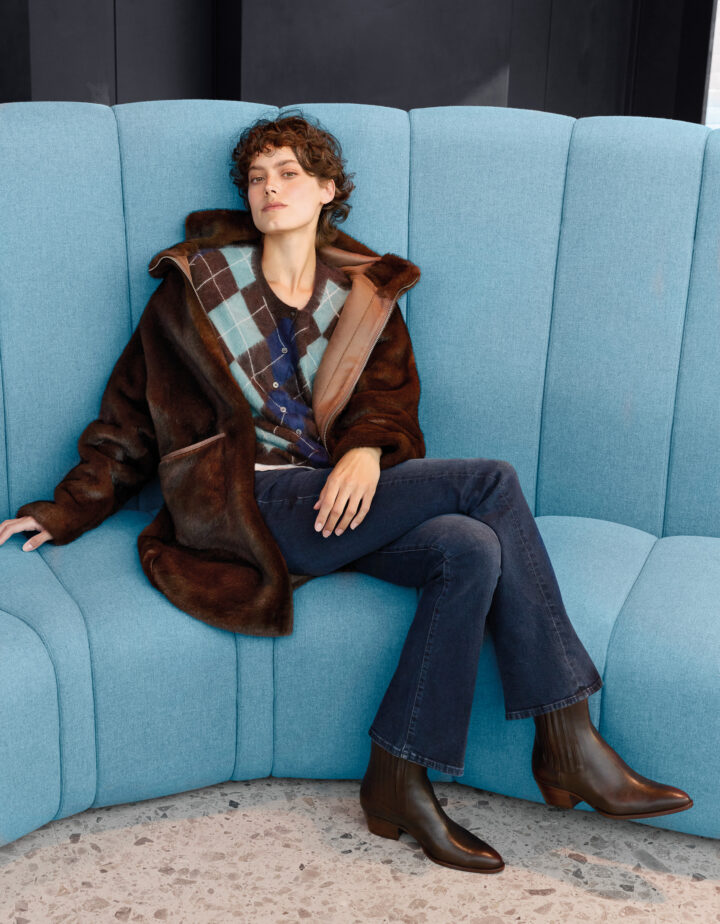 Model trägt eine braune Fake Fur Jacke der Marke Betta Corradi, eine blau-braun gemusterte Weste der Marke The Mercer und eine blaue Jeans der Marke 7 for all Mankind